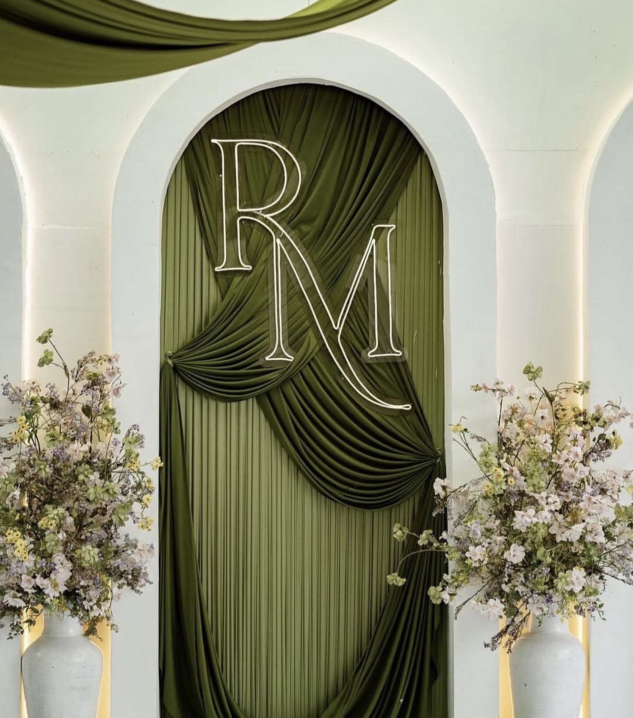Olive-green draped arch with a couple's monogram between two floral urns