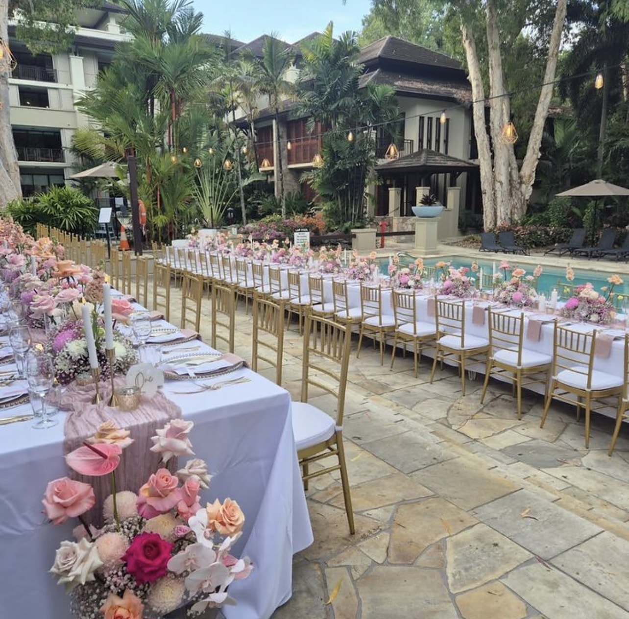 Long poolside dinner table with pink florals stretching across a resort terrace